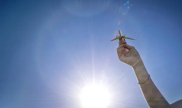 子供の手に高い飛行機の白いおもちゃは、太陽の光の空を飛ぶ。飛行機のフライト、航空機の明るい太陽の下での旅行の背景。空気概念. — ストック写真