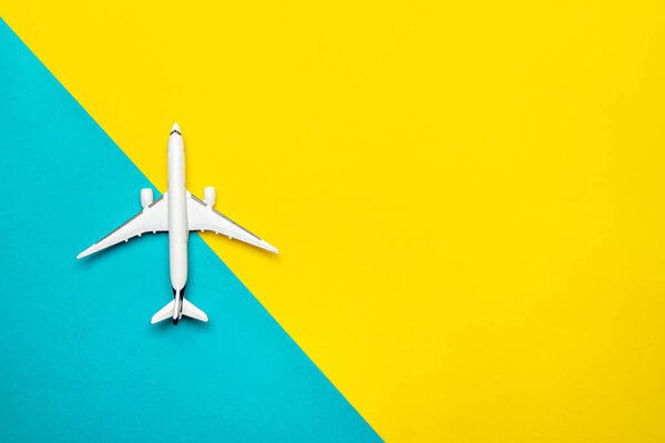 High plane toy in airplane travel concept. White toy aircraft on bright blue and yellow backdrop in top view. Aircraft on air sky background.