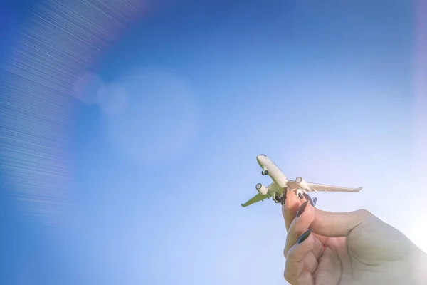 空の日没のおもちゃの飛行機の背景 明るい太陽の光の青い空に女性の手のフライトで飛行機の旅 白い航空機は日光の下で飛ぶ 空気概念 — ストック写真