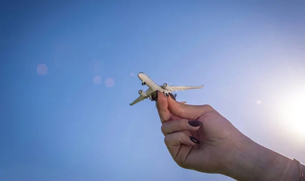 太陽の光の背景に飛行機の白いおもちゃ。女性の手で明るい飛行機は太陽の光の空を旅する。航空機のコンセプトで飛ぶ. — ストック写真