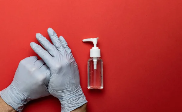 Ασθένεια προστασίας. Hands Using Medical antibacterial sanitizer gel in lab gloves - Εξοπλισμός προστασίας ιών σε κόκκινο φόντο. Διαυγές απολυμαντικό σε φιάλη αντλίας. Προληπτικά μέτρα για τον ιό του κερατοειδούς — Φωτογραφία Αρχείου