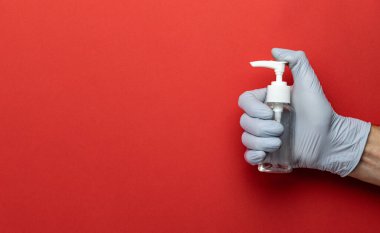 Kırmızıda yıkanan eller. Kırmızı arka planda laboratuvar eldivenlerinde tıbbi dezenfektan jeli kullanmak. Pompa şişesinde dezenfektan var. Coronavirüs salgınının önlenmesi için el temizliği.