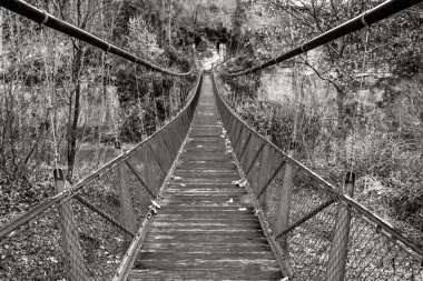 Asma köprü düz perspektif içinde. Ahşap zemin ile demir köprü Nehri üzerinde asılı. Siyah ve beyaz