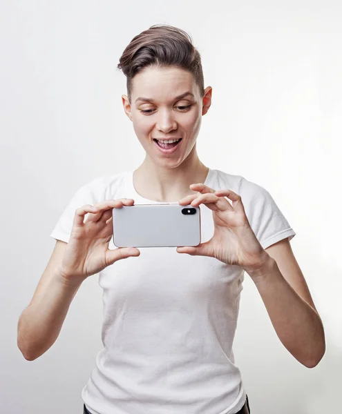 Чудова Азіатська Дівчинка-підліток посміхнувся і зробити фотографію за допомогою передньої камери в її смартфоні, ізольовані на білому фоні. — стокове фото