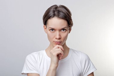 Güzel, sakin, çekici genç kız, çenenin altında bir kol yakın, emin, flört, seductively, giyinmiş Casual, beyaz arka planda bakmak.