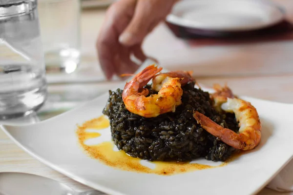 Paella deniz ürünleri Karides masada, yan görünüm beyaz tabakta ile siyah pirinç üzerinden