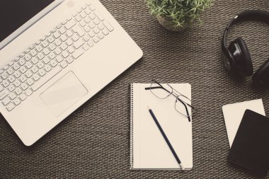 Düz yatıyordu. Bir ofisin laptop, defter, kalem, kulaklık, gözlük, pasaport, kitaplar ve bitki ile Üstten Görünüm