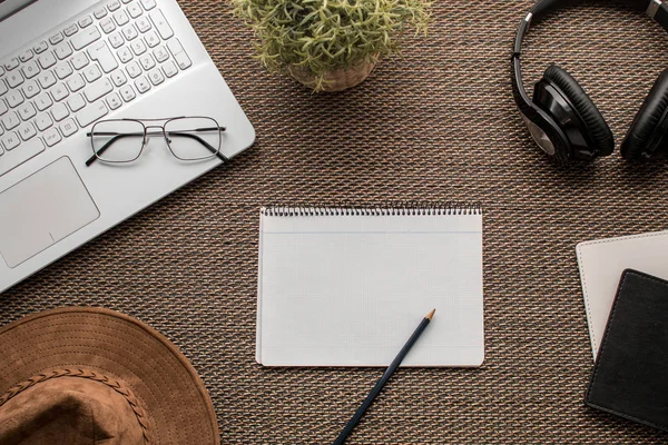 Düz yatıyordu. Bir ofisin laptop, defter, şapka, kalem, kulaklık, gözlük, pasaport, kitaplar ve bitki ile Üstten Görünüm