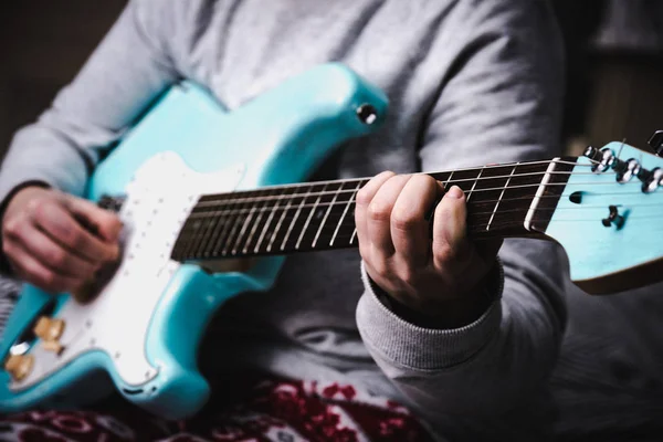 Woman playing blue electric guitar close up at home. Practicing guitar