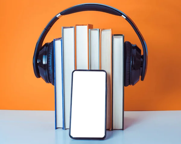 Concepto de audiolibros. Auriculares puestos sobre libro sobre fondo naranja y blanco. Teléfono inteligente. Teléfono móvil . —  Fotos de Stock
