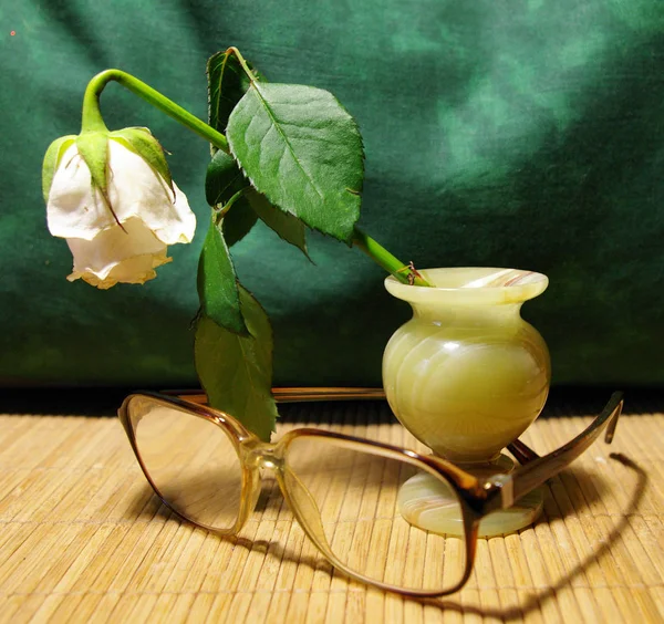 Saman üzerinde doğal taş ve gözlük bir vazoda solmuş gül