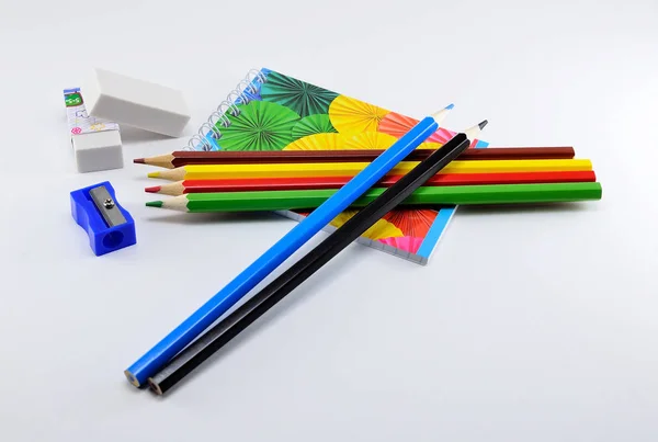 Lápices de colores con gomas de borrar, sacapuntas y bloc de notas sobre fondo blanco . —  Fotos de Stock