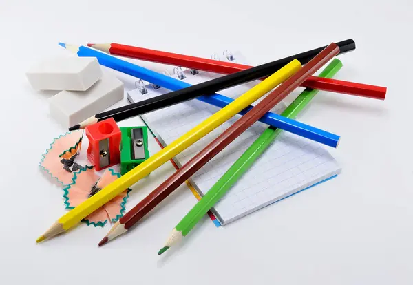 Beyaz arka plan üzerinde renkli kalem silgi, kalemtıraş ve not pad.