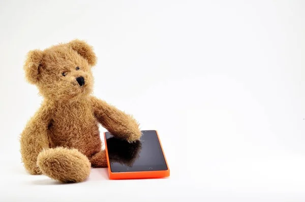 Brinquedo de urso de pelúcia marrom e telefone celular com corpo laranja . Imagens Royalty-Free