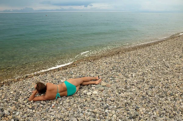 Turkuaz bir mayo bir çakıl plajı sahilde yatan genç bir kız.