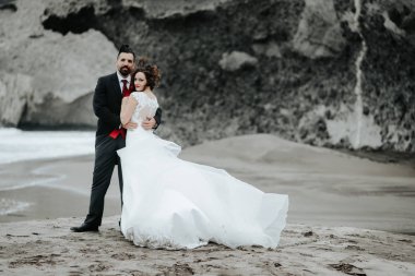 Gelin ve damat sahilde yürüyor. Panoramik görünümü. Sarılma.