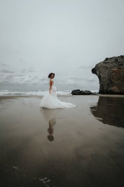 Gelin deniz suya yansıyan sahilde yürüyor. Panoramik görünüm.