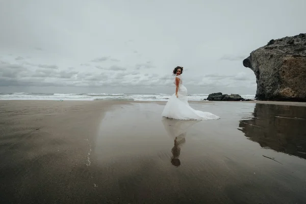 The bride walks on the beach reflected in the sea water. Panoramic view.