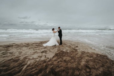 Gelin ve damat sahilde yürüyor. Panoramik görünümü. Sarılma.