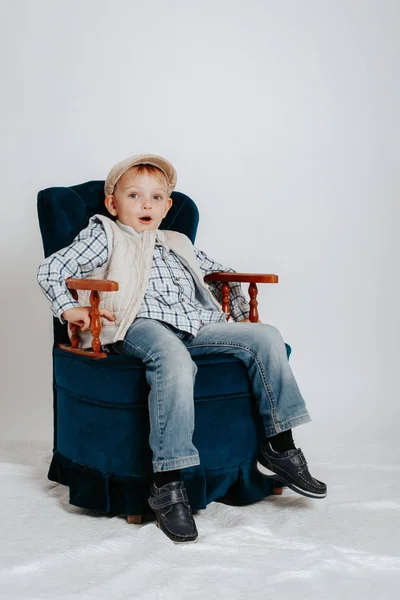 Een jongetje in een cap zit in een luie stoel. — Stockfoto