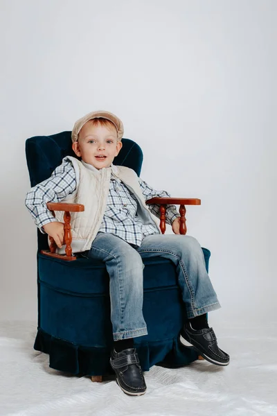 Un niño pequeño en una gorra se sienta en una silla fácil . —  Fotos de Stock