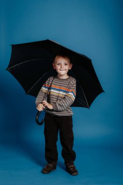 Küçük bir çocuk açık şemsiye altında duran ve gülümseyen.