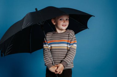 Küçük bir çocuk açık şemsiye altında duran ve gülümseyen.