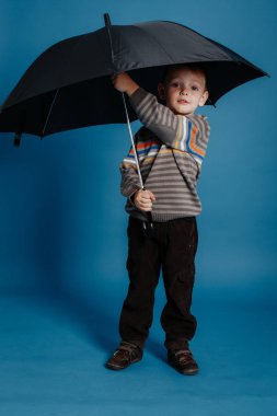 Küçük bir çocuk açık şemsiye altında duran ve gülümseyen.