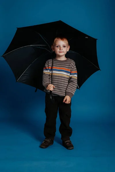 Um menino está de pé sob um guarda-chuva aberto e sorrindo . — Fotografia de Stock
