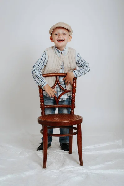 Little boy in a cap sits on a chair and smiles — Stock Photo, Image