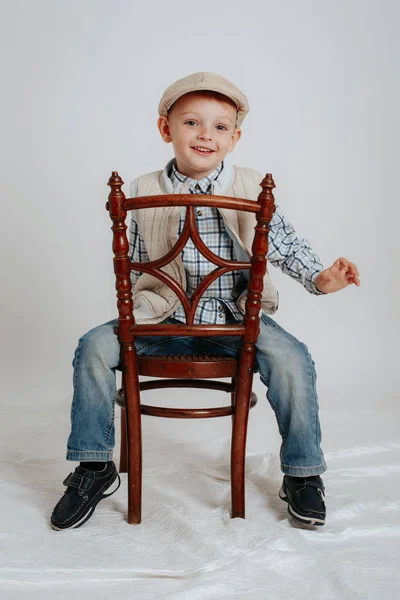 Niño en una gorra se sienta en una silla y sonríe —  Fotos de Stock