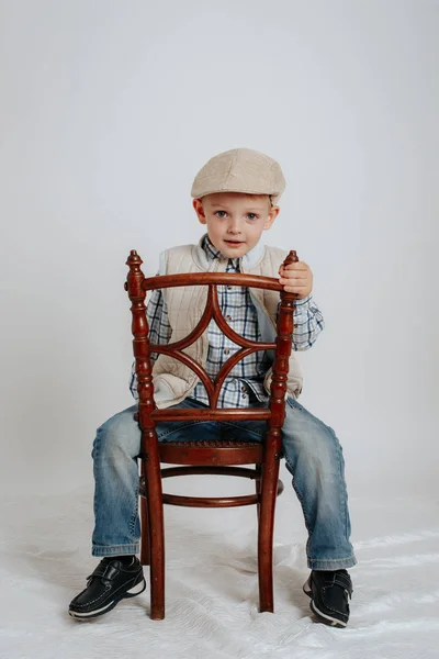 Little boy in a cap sits on a chair and smiles — Stock Photo, Image