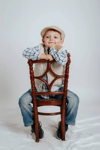 Menino em um boné se senta em uma cadeira e sorri — Fotografia de Stock