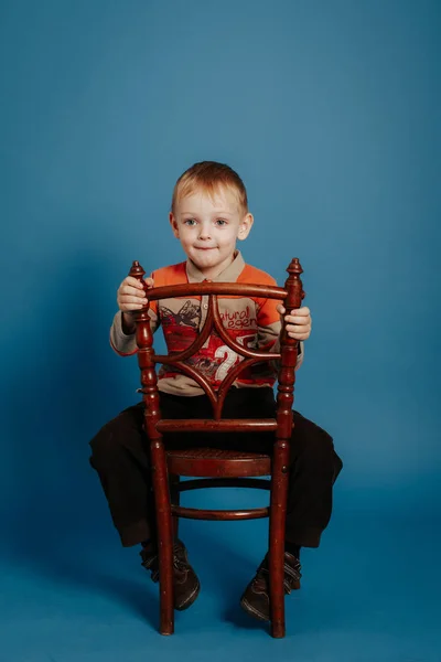 Mały chłopiec w czapce siedzi na krześle i uśmiecha się. — Zdjęcie stockowe