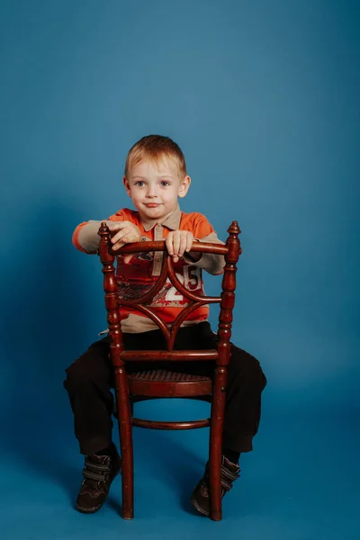 A little boy in a cap sits on a chair and smiles. — Stock Photo, Image