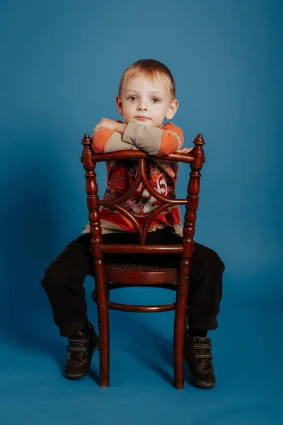 A little boy in a cap sits on a chair and thinks. — Stock Photo, Image