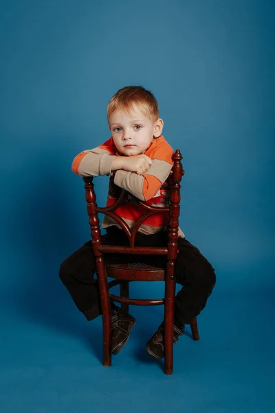 En liten pojke i ett tak sitter på en stol och tänker. — Stockfoto