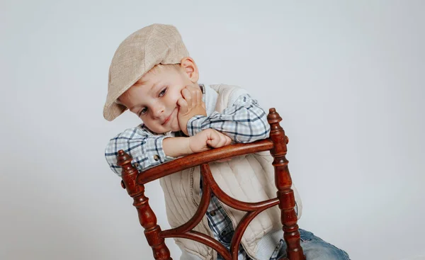 Un niño en una gorra se sienta en una silla y piensa: . — Foto de Stock