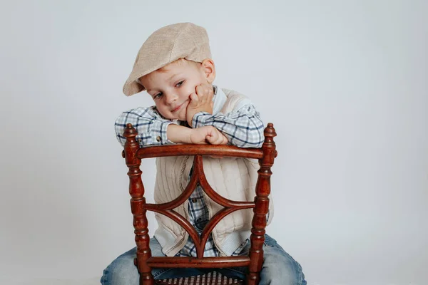 Un niño en una gorra se sienta en una silla y piensa: . —  Fotos de Stock