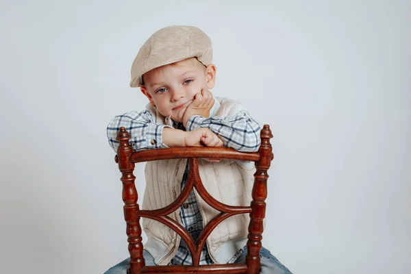 A little boy in a cap sits on a chair and thinks. — Stock Photo, Image