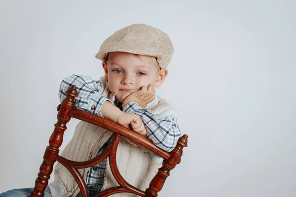 Een jongetje in een cap zit op een stoel en denkt. — Stockfoto