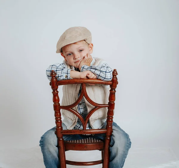 Un niño en una gorra se sienta en una silla y piensa: . —  Fotos de Stock