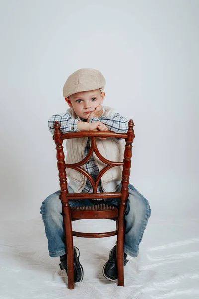 A little boy in a cap sits on a chair and thinks. — Stock Photo, Image