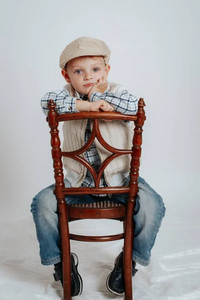 Een jongetje in een cap zit op een stoel en denkt. — Stockfoto