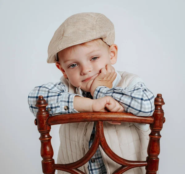 Ein kleiner Junge mit Mütze sitzt auf einem Stuhl und denkt. — Stockfoto