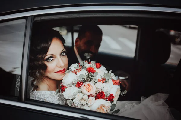 Koyu renk saçlı gelin düğün gününde bir buket ile siyah arabada oturur. — Stok fotoğraf