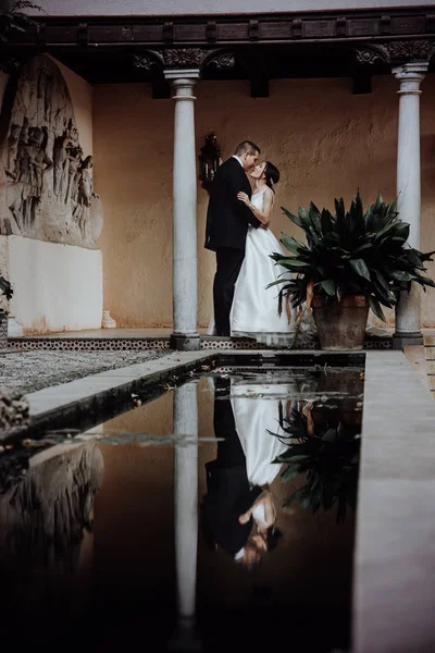 Hochzeitspaar spiegelt sich im Wasser, umarmt sich und schaut sich an. — Stockfoto