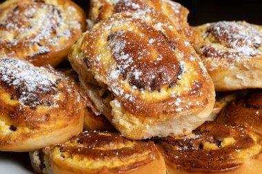 Süzme peynirli ve kuru üzümlü köfteler bir tabakta yığılmış. Peynirli kek, süzme peynirli turta. Üzerine pudra şekeri serpiştirilmiş köfteler. Yakın çekim görünümü