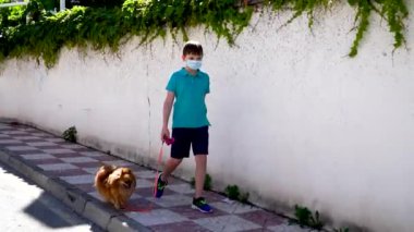 Coronavirus covid-19 konsepti. Tıbbi maskeli küçük bir çocuk bir köpekle yürüyor. Dışarıda tıbbi maske takan çocuklar. Yeni gerçeklik.