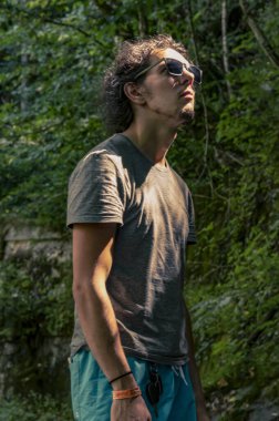 Dışarı çık. Güneş gözlüklü genç bir adam çevresindeki doğaya bakar. Gün ışığı yüzüne vurur.